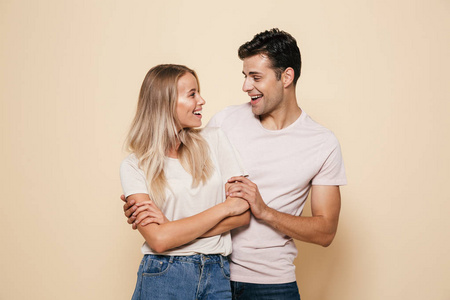 一对微笑的年轻夫妇站在一起, 在米色背景, 牵手的肖像