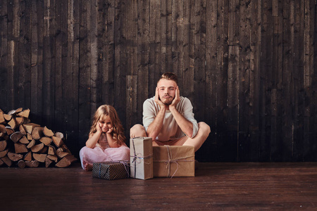 不安的父亲和女儿坐在地板上, 在空房间的礼物在一个木墙上