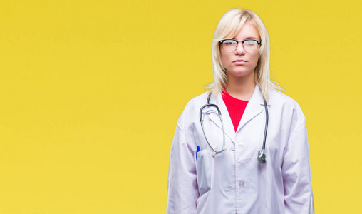 年轻美丽的金发医生妇女穿着医疗制服在孤立的背景下, 面部表情严肃。简单而自然地看着相机