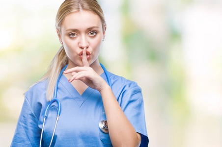 年轻的金发外科医生妇女在孤立的背景要求安静的手指在嘴唇上。沉默与秘密概念
