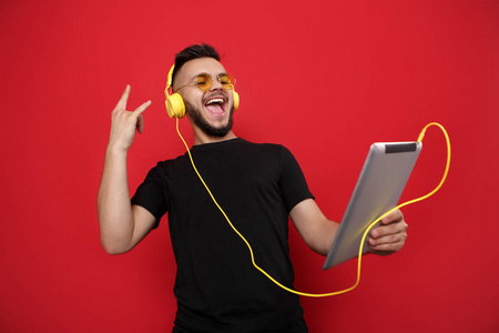 亮胡子男子在黄色的太阳镜和黑色 t恤听音乐的平板上的快乐脸上的红色背景