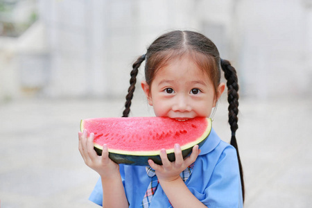 可爱的小亚洲儿童女孩在学校制服享受吃新鲜切片西瓜