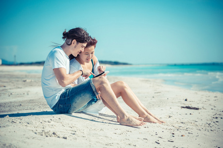 年轻的夫妇在海边与数字平板电脑