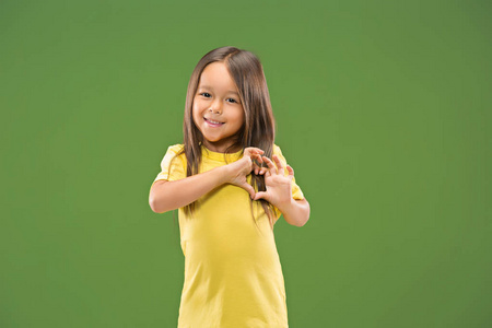 美丽的微笑的青少年女孩做的形状的心脏与她的手在绿色背景