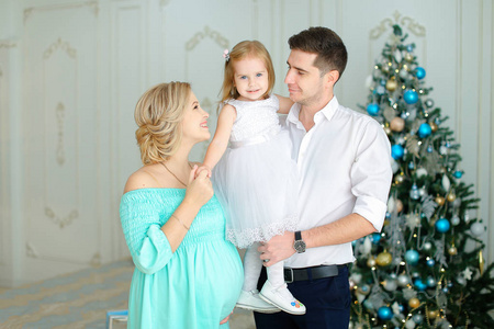 怀孕的欧洲妇女站在丈夫身边, 把小女儿留在圣诞树旁。