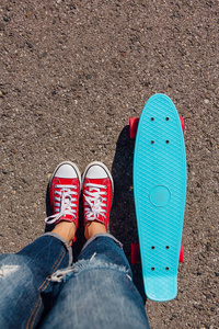 在红色运动鞋的女孩的脚关闭骑在蓝色塑料便士滑板与粉红色的车轮。都市风光, 城市生活。运动, 健身生活方式