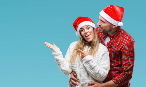 年轻夫妇在爱戴着圣诞节帽子在孤立的背景惊讶和微笑的相机, 而用手和手指指着
