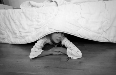 拖鞋在床底下小女孩躲在家里的床底下的肖像照片