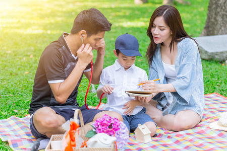 亚洲青少年家庭教儿子家庭作业在户外公园野餐