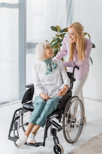 在疗养院与坐在轮椅上的高级女子交谈的年轻女子