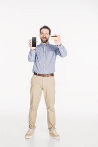 微笑胡子的人显示的智能手机与空白屏幕和信用卡在手上孤立的白色