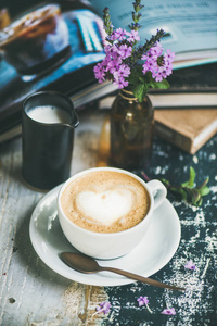 古典泡沫卡布奇诺咖啡在杯子与牛奶和花在质朴的木桌