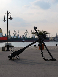 一个大的海锚装饰着港口的步行部分, 背景是港口的水域货轮和港口吊车