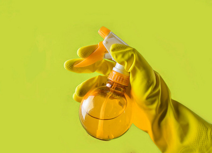 一只戴着黄色橡胶手套的手拿着一个红色的喷雾瓶在绿色的背景