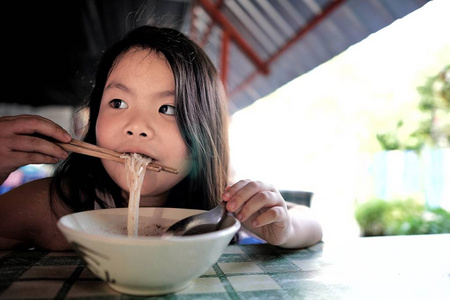 亚洲小可爱的女孩的肖像吃美味的泰国面条自己的筷子。食物, 家庭, 童年概念