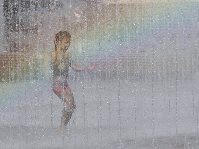 在彩虹的光芒中, 一个女孩快乐地奔跑, 沐浴在城市的喷泉里。炎热的阳光天气。闲暇时孩子们无忧无虑的游戏。城市基础设施。清爽的水溅