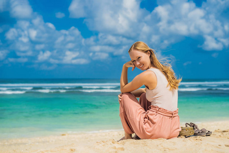 年轻的妇女坐在沙滩上, 欣赏绿松石水在惊人的梅拉斯蒂海滩, 巴厘岛, 印度尼西亚