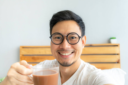 愉快的亚洲人与眼镜和白衬衫单数自己喝热咖啡