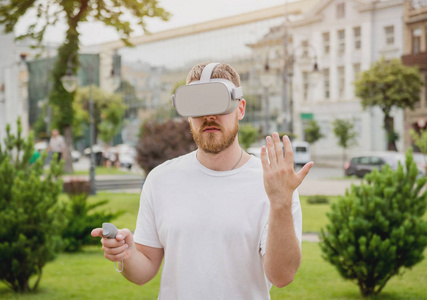 年轻的金发胡子男子玩游戏戴着虚拟现实眼镜在街上。Vr 耳机