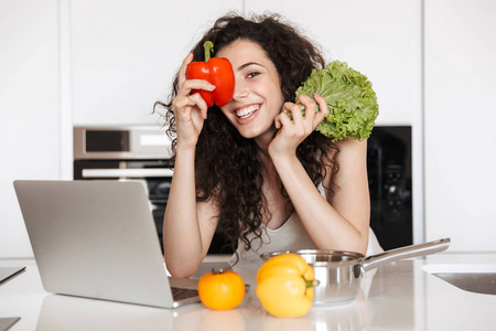 快乐的女人的照片, 在厨房做饭和阅读食谱从笔记本电脑的情人举行绿色萨拉特和甜纸
