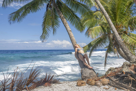 放松的女人躺在热带海滩上的椰子棕榈树上。躺在海边的棕榈树上的年轻美丽的女人。暑假概念图