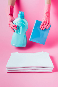 橡胶手套中女清洁工的部分观点持有洗衣液和洗衣粉的清洁白色 t恤衫, 粉红色背景