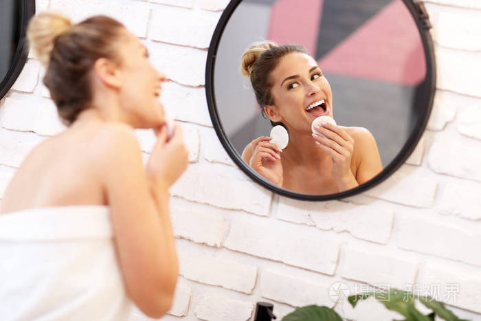 年轻妇女清洁面孔在浴室镜子