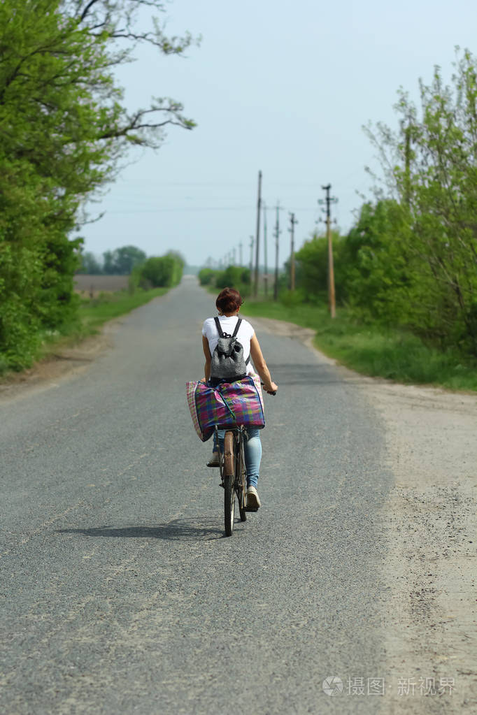 骑着一辆旧的生锈的自行车沿着乡间小路的年轻女子