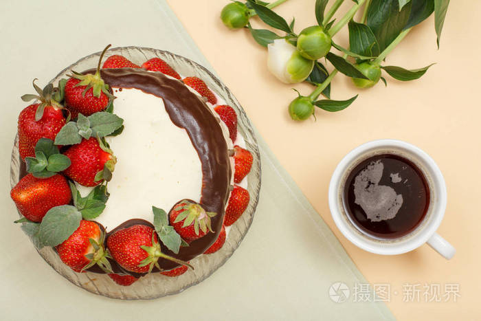 自制的巧克力蛋糕, 装饰着新鲜的草莓和薄荷的叶子在玻璃盘子, 杯咖啡和牡丹花束的灰色和米色的背景。顶部视图