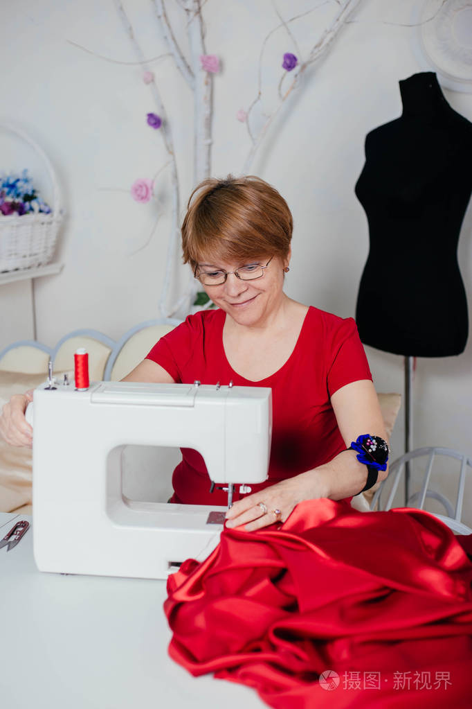一个穿红衣服的女裁缝在缝纫机上缝制.工作室, 裁剪过程