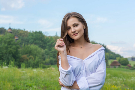 美丽的微笑年轻妇女在白色衬衣站立在农村风景背景在夏天
