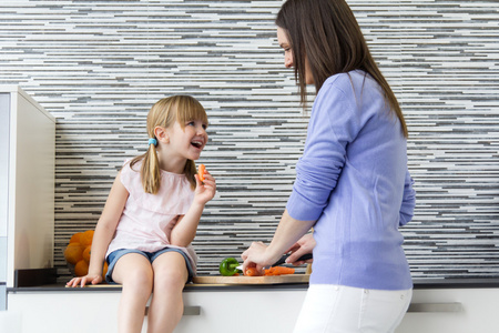 年轻女人和小女孩在厨房里吃胡萝卜