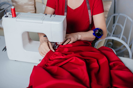 一个穿红衣服的女裁缝在缝纫机上缝制。工作室, 裁剪过程