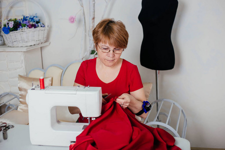 一个穿红衣服的女裁缝在缝纫机上缝制。工作室, 裁剪过程