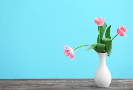 花瓶与美丽的郁金香在木桌反对颜色背景