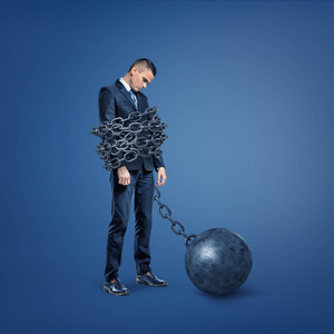 站在宽一个悲伤失望的商人站在一条被铁棍锁着的宽金属链的束缚下照片