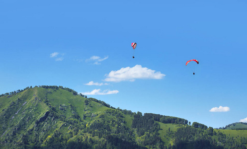 在阳光明媚的日子, 滑翔伞飞过山上。