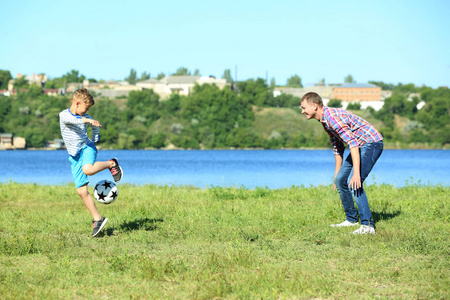 快乐的父亲和儿子在河边踢足球