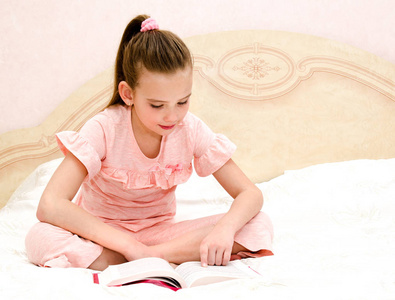 可爱的小女孩子正在读一本书在床上