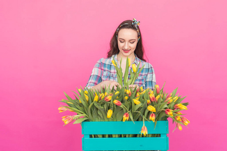 快乐的高加索年轻妇女与盒黄色郁金香粉红色背景