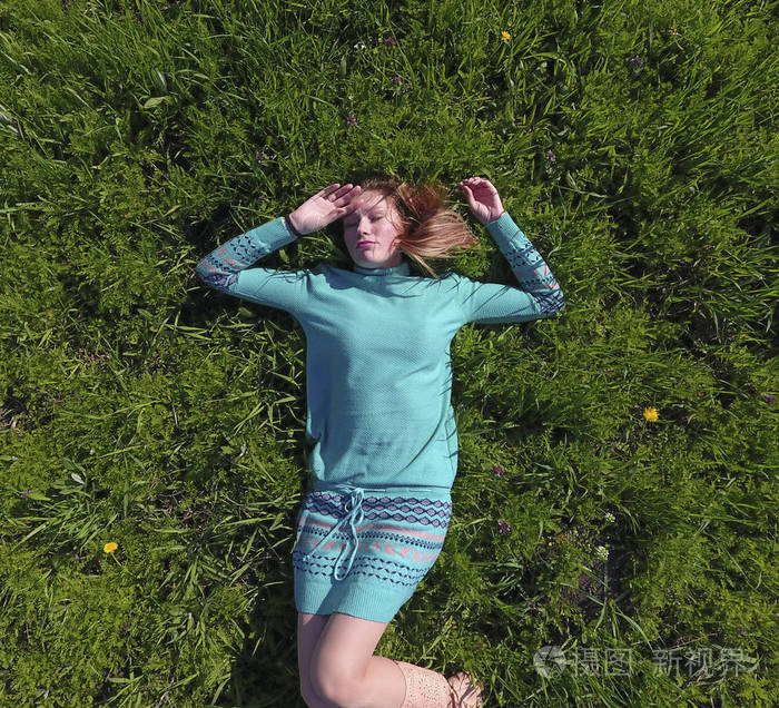 那女孩躺在草坪上的一条绿松石裙上.美丽的女孩躺在草地上照片-正版商
