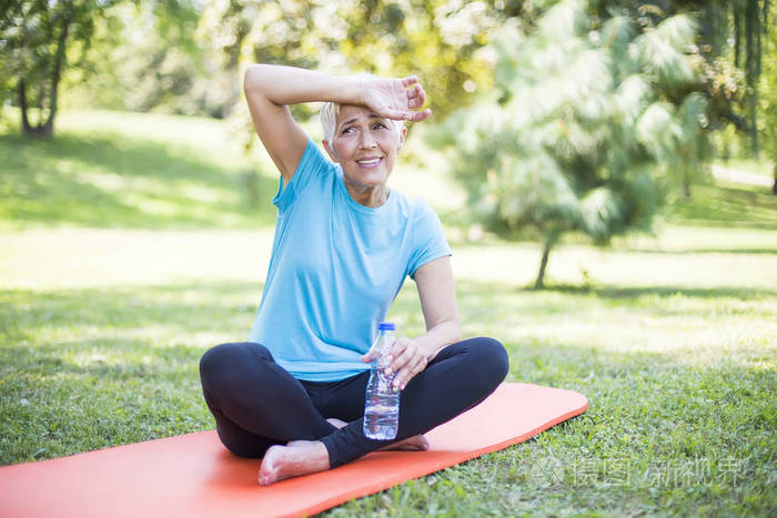 高级运动女性坐在外面的垫子上, 锻炼后休息