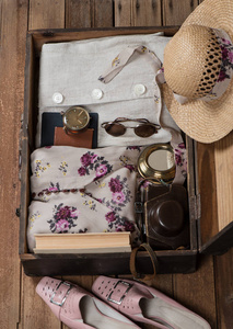 打开袋的顶部视图与夏天 clothefor 妇女和帽子, 照相机, 步进, 太阳镜, 时钟和书在老木地板上