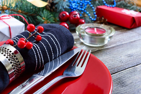 圣诞餐桌设置。红色盘子叉子刀蜡烛餐巾纸礼物树枝上的圣诞树上的木制背景。圣诞新年假期明信片