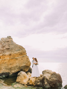 新郎的全长视图拥抱新娘回来, 亲吻她的头, 而站在悬崖之间的海