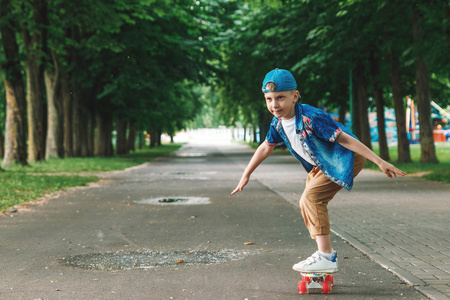 一个小城市男孩和一个滑板。一个年轻人骑着滑板坐在公园里。城市风格。城市的孩子。孩子学会骑滑板
