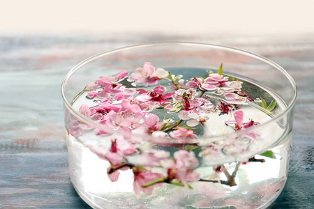 玻璃碗与水和盛开的花朵在木桌上, 特写