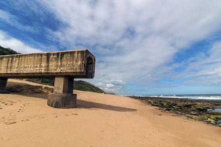 在 Garvies 海滩上的岩石海岸线和蓝色多云海岸景观的混凝土排水管道延伸到沙滩上, 南非德班的悬崖上。