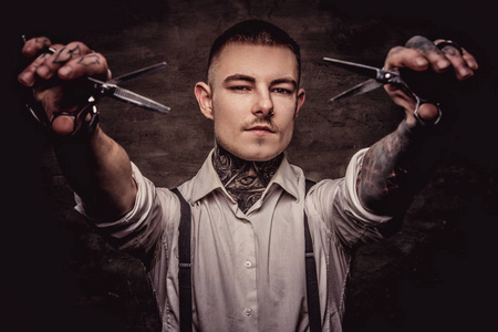 戴着吊带衫的老式纹身理发师的画像上拿着一把剪刀.