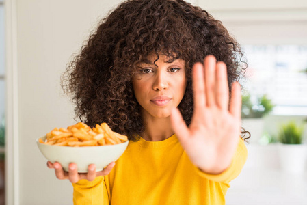 非洲裔美国妇女拿着薯片在家里与张开手做停止标志认真和自信的表达, 防御姿态